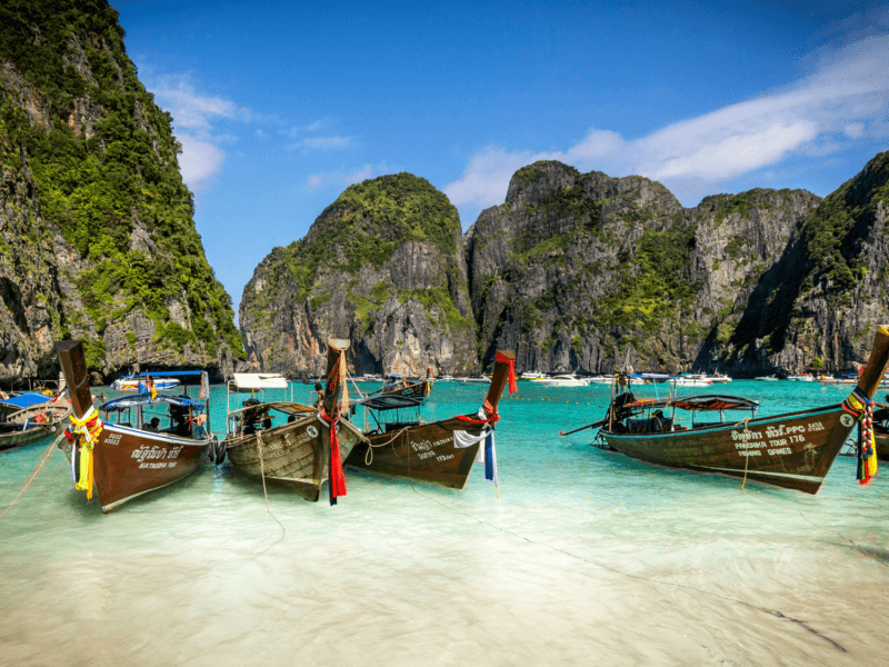 Longtail boats floating in the turquoise waters of Phi Phi Island, surrounded by towering limestone cliffs. A picturesque destination in Phuket.