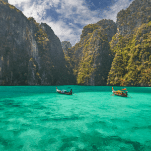 Longtail boats floating in the turquoise waters of Phi Phi Island, surrounded by towering limestone cliffs. A picturesque destination in Phuket.