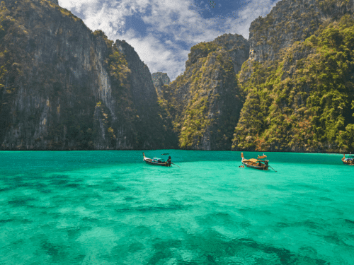 Longtail boats floating in the turquoise waters of Phi Phi Island, surrounded by towering limestone cliffs. A picturesque destination in Phuket.