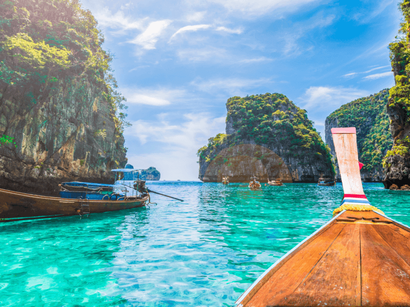 Traditional longtail boat entering a stunning lagoon at Phi Phi Island, surrounded by turquoise waters, green cliffs, and a clear blue sky.