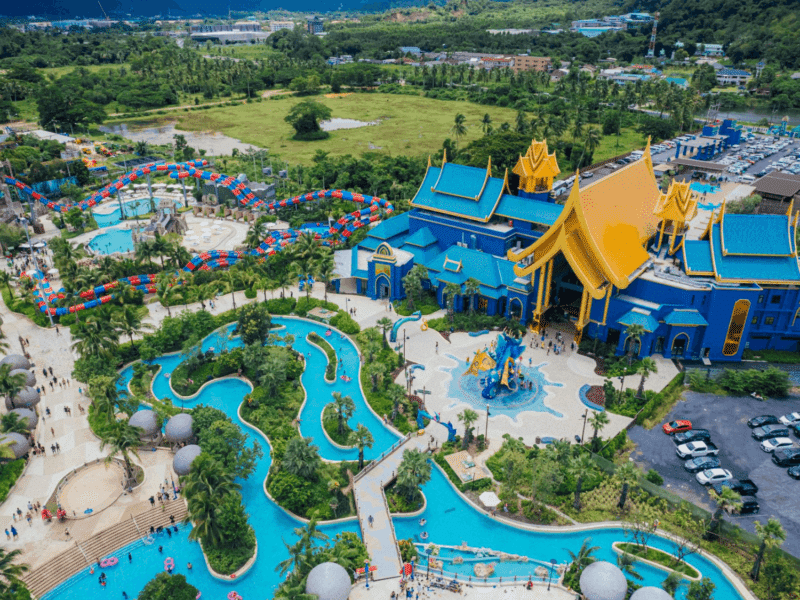 A breathtaking aerial view of Andamanda Water Park in Phuket, showcasing vibrant slides, a lazy river, lush greenery, and the grand blue-and-gold entrance building.