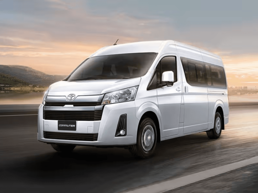 Modern white Toyota commuter van driving on a highway during sunrise, offering premium airport transfer services.