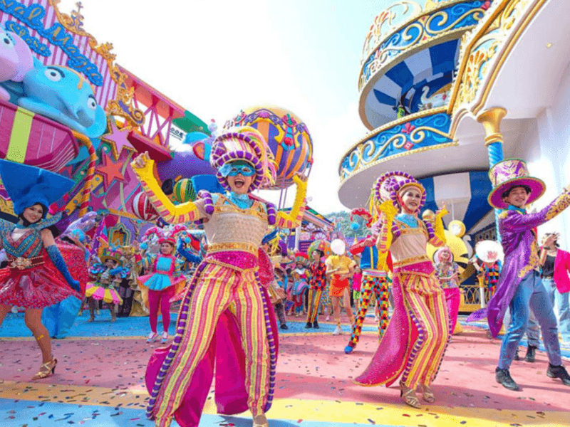 Performers in vibrant costumes dancing during a colourful daytime celebration at Carnival Magic in Phuket.