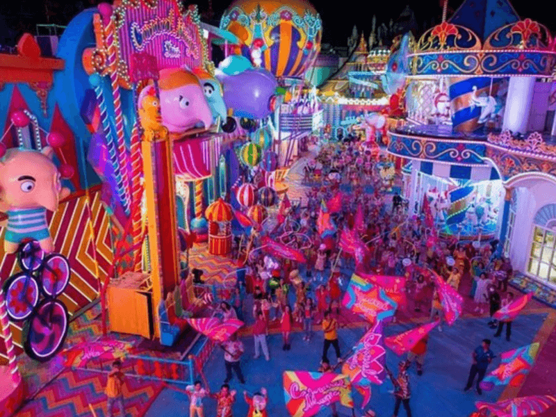 A vibrant night parade at Carnival Magic in Phuket with colourful floats, flags, and cheerful performers under bright neon lights.