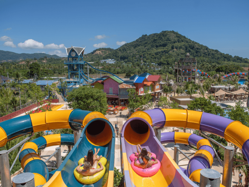 Visitors enjoying a colorful water slide at Andamanda Water Park Phuket with scenic mountain views in the background.