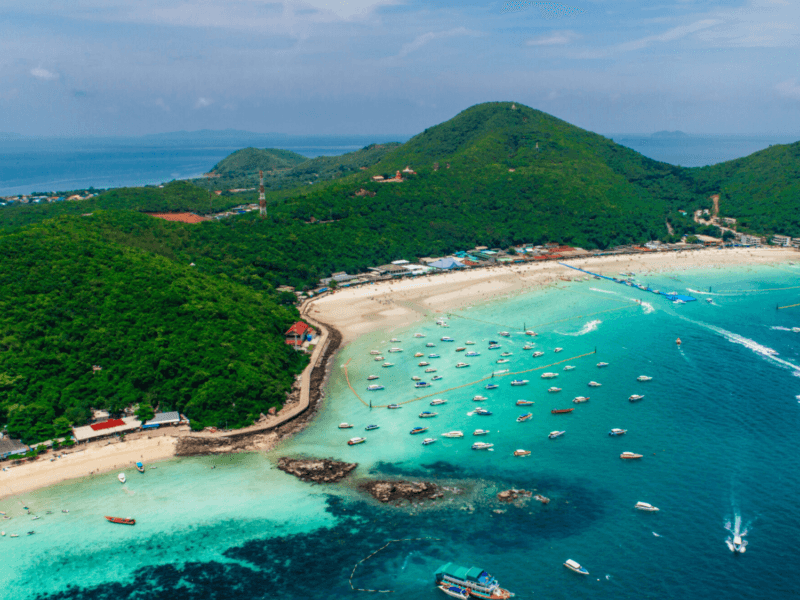 A stunning aerial view of Coral Island, featuring turquoise waters, lush green hills, and a vibrant coastline dotted with boats. Ideal for island tours and beach adventures.