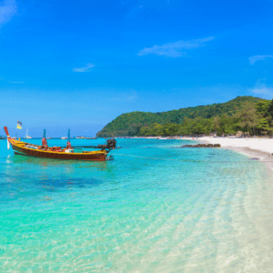 Coral Island tour: Crystal-clear waters with a traditional longtail boat at Coral Island, Phuket, Thailand, surrounded by lush greenery and blue skies.