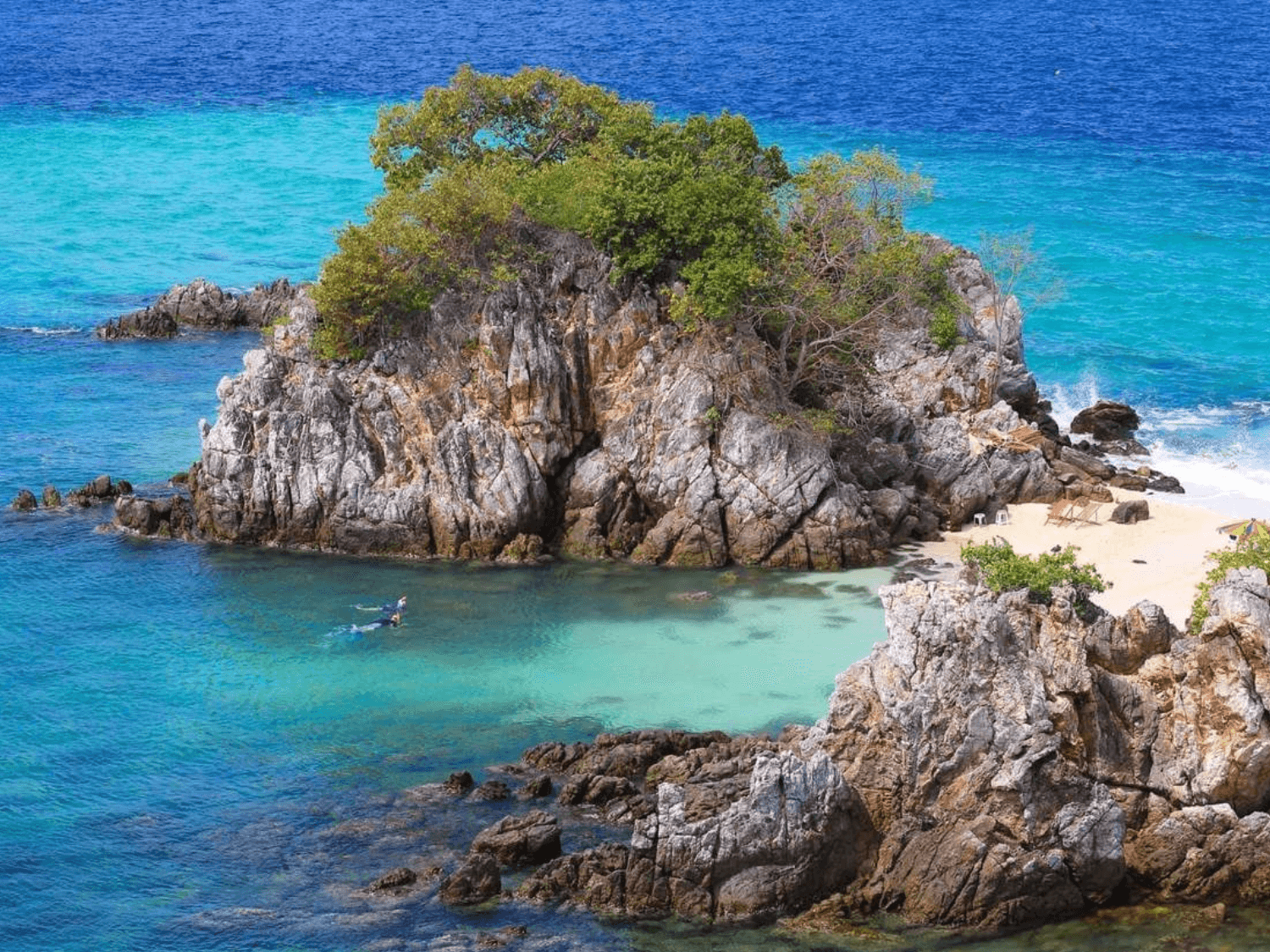 A hidden cove on Khai Island surrounded by rocky cliffs, turquoise waters, and lush greenery, offering a peaceful tropical retreat.