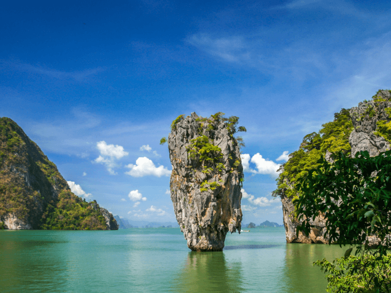 Iconic limestone karst at James Bond Island under a bright blue sky with lush greenery and tranquil waters.