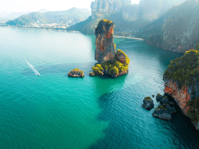 Breathtaking aerial view of Krabi Island with a speedboat gliding across turquoise waters surrounded by dramatic cliffs.