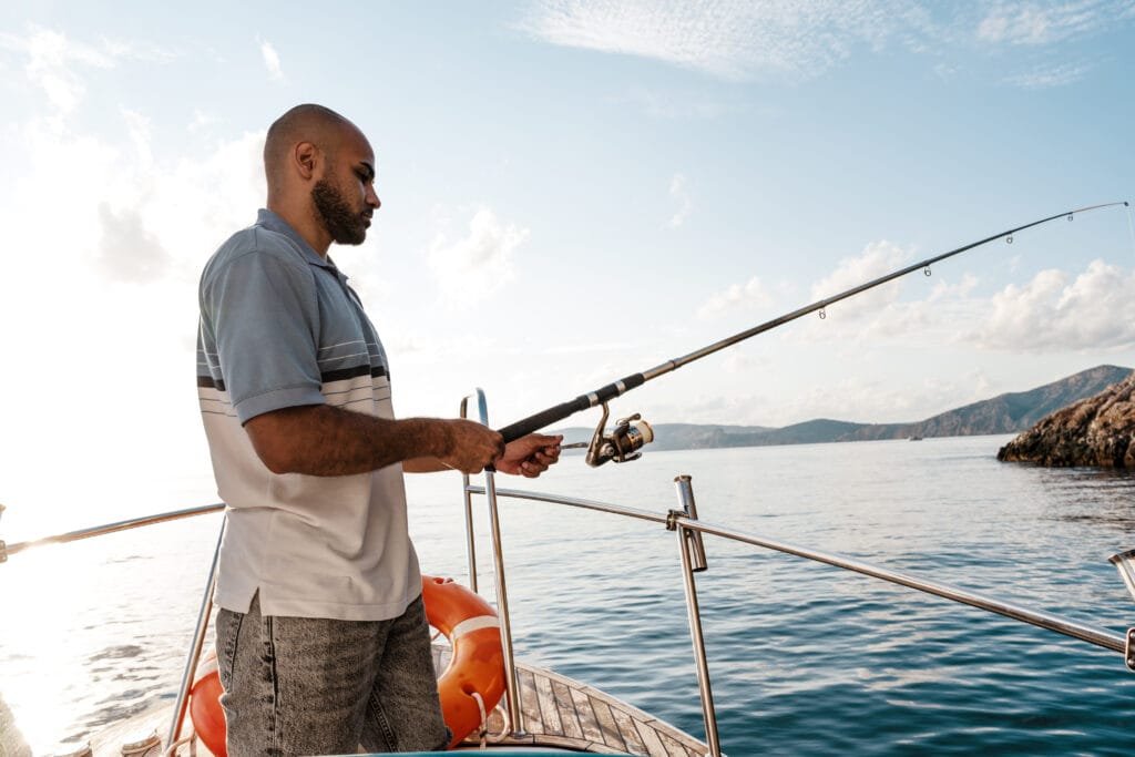 private charter fishing in Phuket:  A man fishing from a luxury boat with a scenic backdrop of calm waters and rocky cliffs.