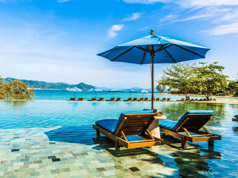 Luxurious poolside lounge chairs with blue umbrellas overlooking the turquoise waters and serene beach of Naka Noi Island.