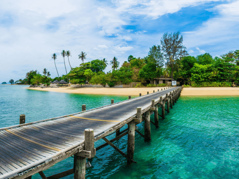 Wooden pier leading to the serene beach of Naka Noi Island with lush greenery and turquoise waters.