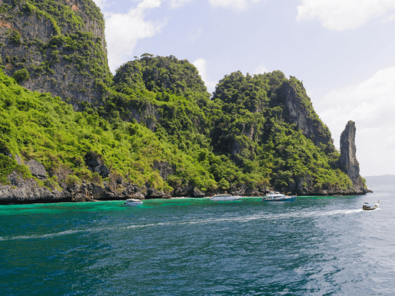 The towering lush cliffs of Phi Phi Islands surrounded by emerald-green waters and small boats cruising nearby.