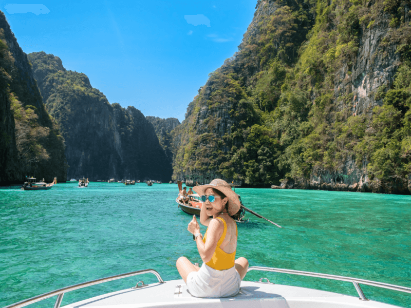 A tourist enjoying a speedboat tour in the turquoise waters of Phi Phi Islands, surrounded by lush cliffs and longtail boats.