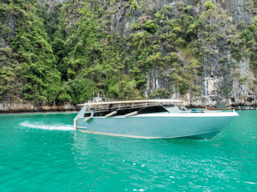 Private Charter Phi Phi: A sleek private speedboat cruising through turquoise waters near the lush cliffs of Phi Phi Islands in Thailand.