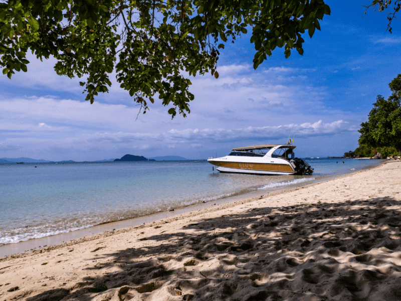 A private speedboat anchored on a secluded sandy beach in Krabi, surrounded by calm turquoise waters and lush greenery.