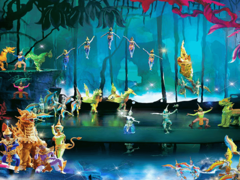 Performers in vibrant costumes enact a forest-themed mythical scene at Siam Niramit Phuket, with glowing creatures and an enchanting stage backdrop.