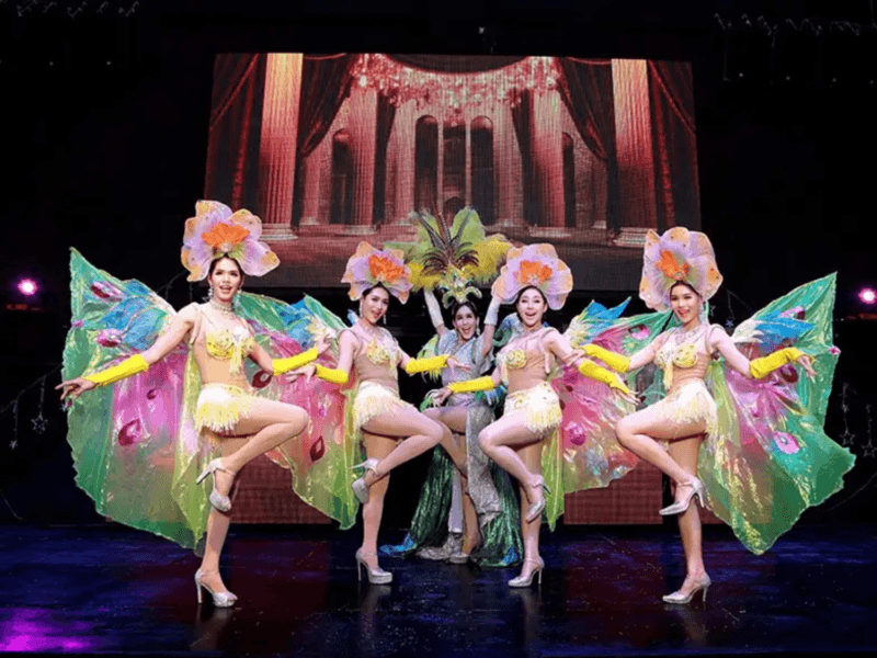 Performers at the Simon Cabaret Show in Phuket, dressed in butterfly-inspired costumes with vibrant colours, posing elegantly on stage.