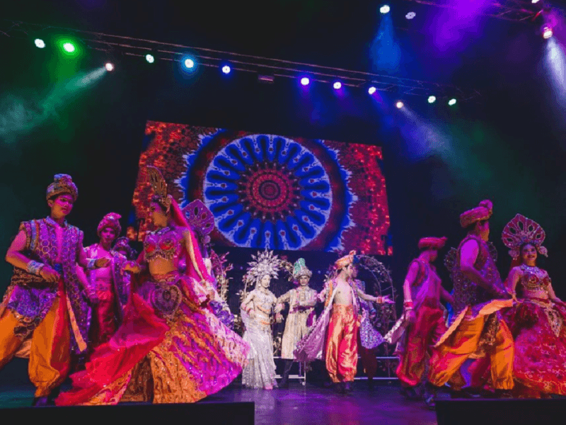 Performers at the Simon Cabaret Show in Phuket, dressed in vibrant and exotic costumes, dancing under dramatic stage lighting.