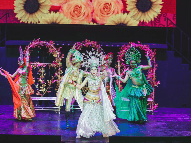 Performers at the Simon Cabaret Show in Phuket dressed in vibrant cultural costumes, dancing on a beautifully decorated stage.