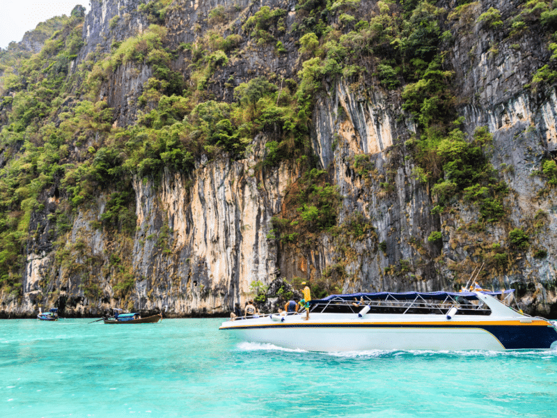 A private speedboat cruising along turquoise waters near the towering limestone cliffs of Phi Phi Islands.