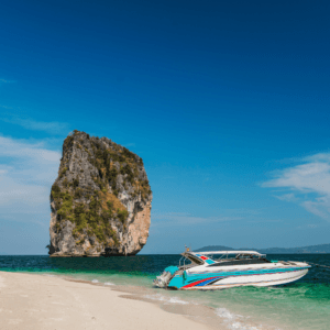 A private speedboat anchored on a pristine white sand beach with a towering limestone island in the background at Phi Phi Islands.