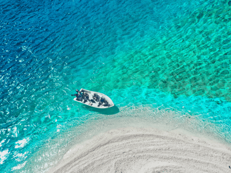 Aerial view of a speedboat on crystal-clear turquoise water near a sandy beach, offering a serene and picturesque setting.