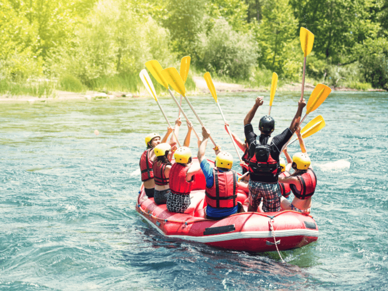 A group of rafters raising their paddles in celebration during an exciting white water rafting adventure on a serene river in Phuket.