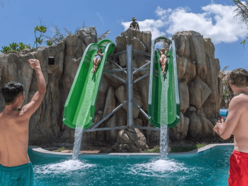 Visitors enjoying the thrilling green water slide at Andamanda Water Park Phuket, surrounded by rocky scenery and a clear blue sky.