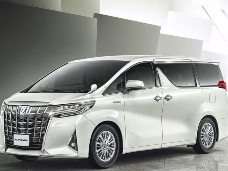 Front-side view of a white Toyota Alphard luxury minivan in a sleek indoor setting.