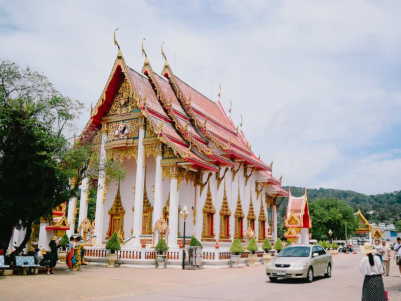 Exterior view of Wat Chalong, a famous Buddhist temple in Phuket, Thailand, with intricate gold details and a red-tiled roof under a bright sky.