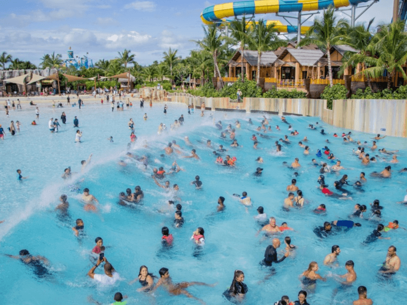 Families and groups enjoying the wave pool at Andamanda Water Park Phuket, with vibrant water slides and palm trees in the background.