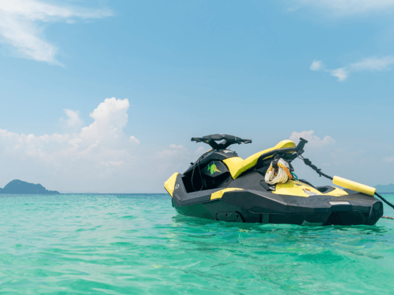 Yellow jet ski floating in the crystal-clear blue waters of Phuket with a scenic island backdrop.