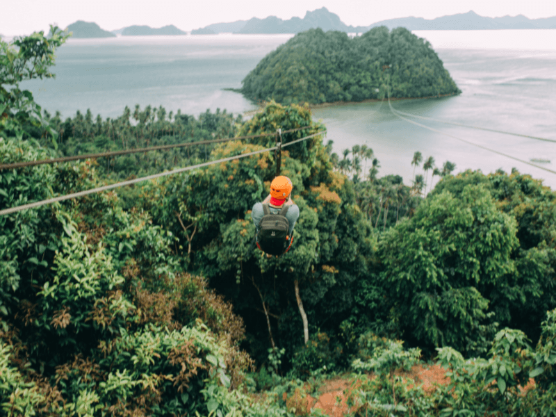 Back view of a person ziplining through lush green forests with breathtaking island and sea views in Phuket.