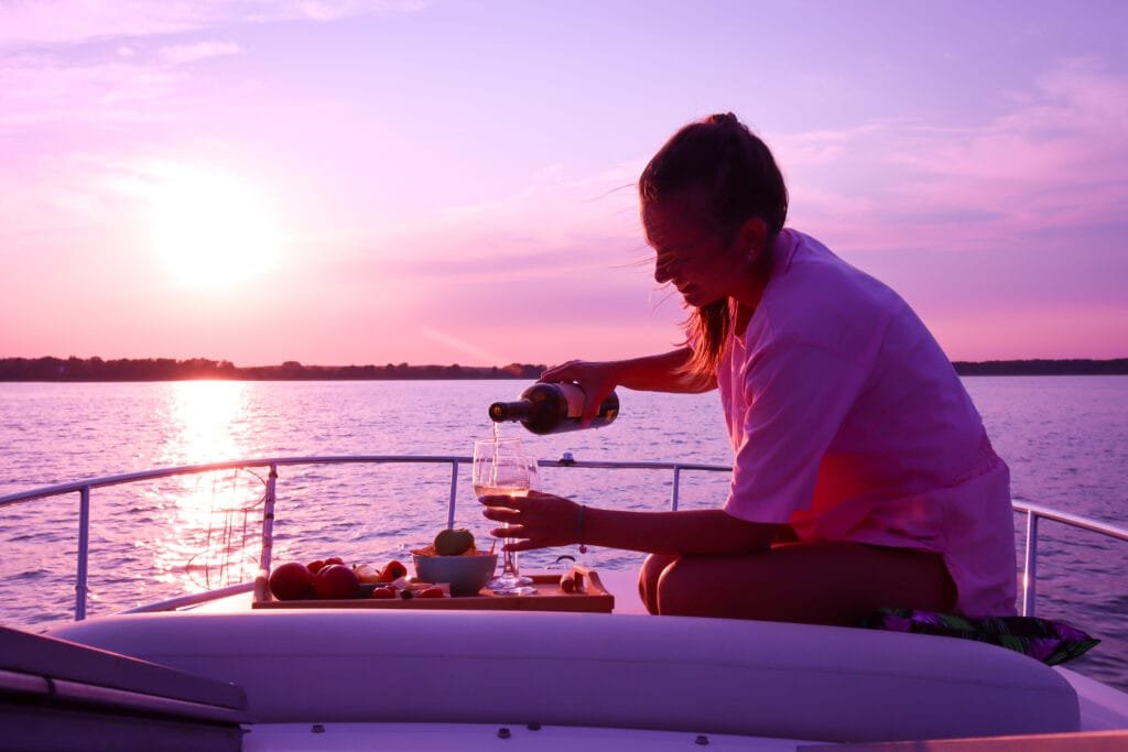 sunset viewing spots in Phuket: A woman pours wine into a glass on a boat during a picturesque sunset over calm waters.